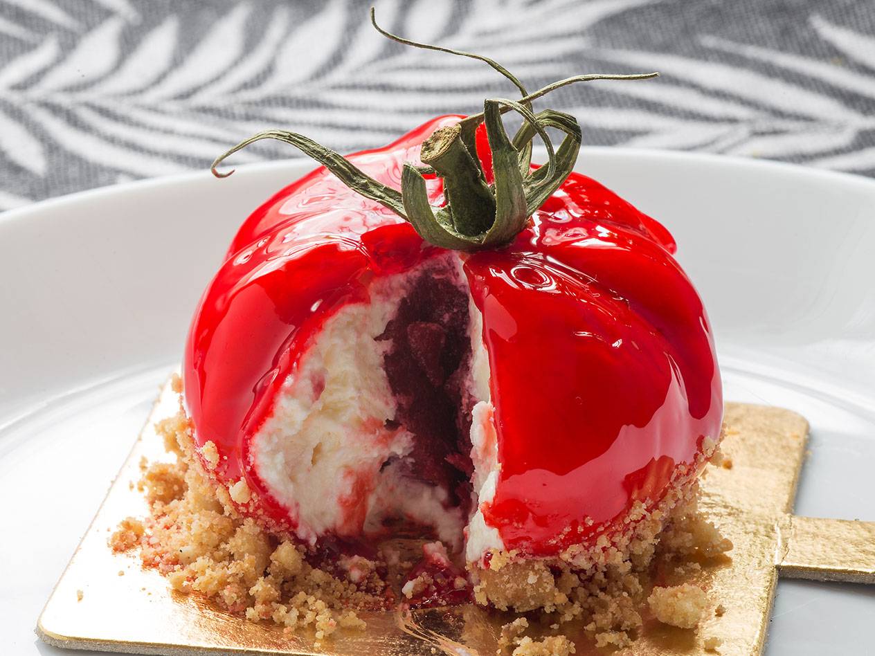 En röd tomatformad dessert med en skiva bortskuren, som visar en krämig fyllning och en kexbotten.