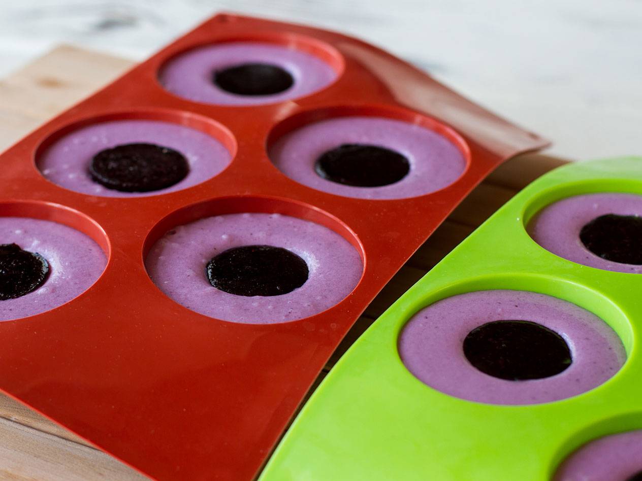 Röda och gröna silikonformar fyllda med lila smet och en mörk kaka i mitten.